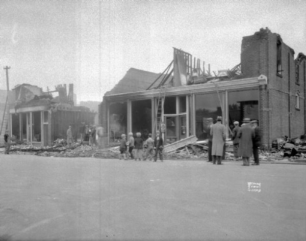 Fire scene from the west end, showing ruins of the Lins and Hood hardware and furniture store, a pool hall, and confectionary store, with adults and children looking on.