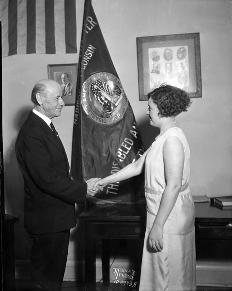 Mayor Albert Schmedeman holding the hand of Nina Westbury in front of the Morris O. Togstad Chapter 2 Disabled American Veterans of the World War flag.