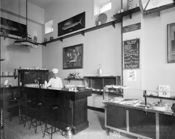 McNeil's Tap Room, Park Hotel, 22 S. Carroll Street. Menu and prices are posted on the wall. A man wearing a tall chef's cap is standing behind the counter.