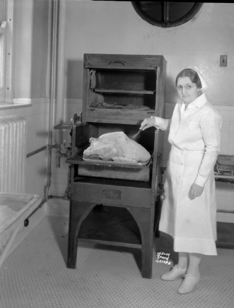 Blanche Taylor, dietician at Madison General Hospital, testing turkey in commercial oven in hospital kitchen.