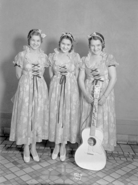 "Three Little Maids," group portrait of three women, all standing, one holding a guitar, who performed with the WLS Barn Dance.
