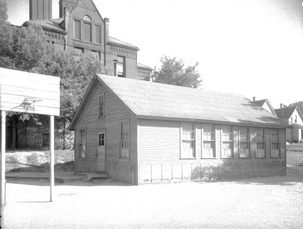 Small wooden barracks building with a portion of the old Lapham School, 1436 E. Dayton Street, in the background.