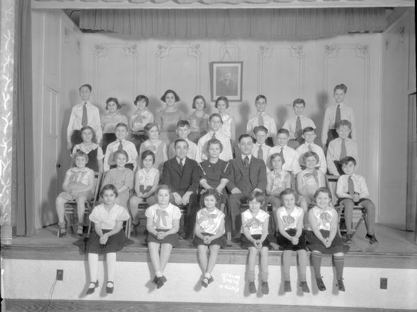 Jewish Children & Adults Group portrait of Jewish children and teachers sitting on a stage in the Workmen's Circle Labor Lyceum, 41 - 43 N. Mills Street at Spring Street, Greenbush. They are going to present a Jewish play "Chanukah Money."