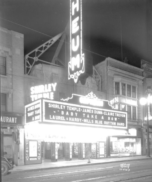 View from street towards the Orpheum Theater marquee, which reads: "Shirley Temple - James Dunn - Claire Trevor in Baby Takes a Bow, Laurel & Hardy - Mills Blue Rhythm Band." The Thom McAn Shoe store is next door at 214 State Street.