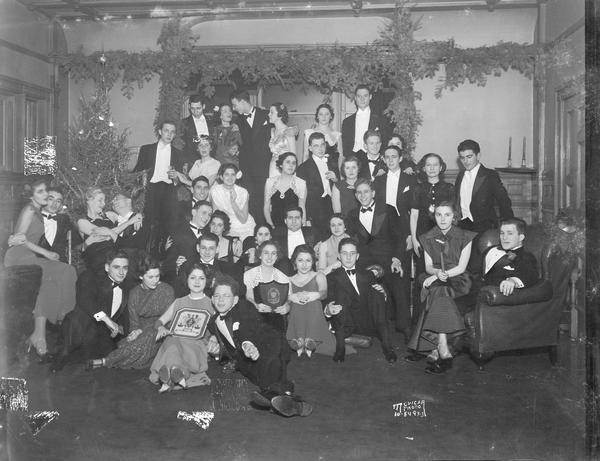 A group portrait of the Zeta Beta Tau Christmas formal, 216 Langdon Street, with two girls holding ZBT plaques with its crest.