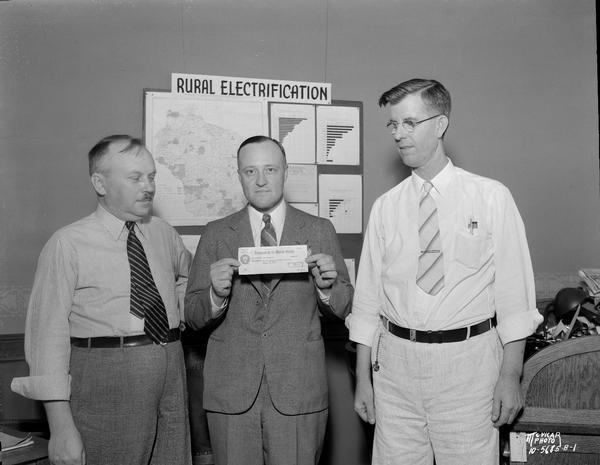 Three men displaying $5000 check issued by U.S. Treasury Dept. to Richland Cooperative Electric Association for Rural Electrification Program.