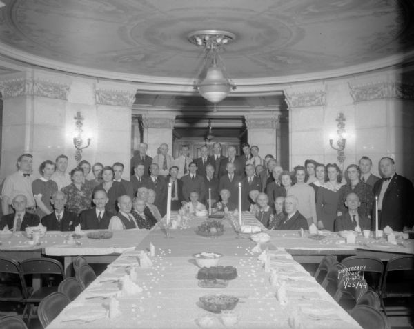 Group portrait of those in attendence at a dinner to honor 14 retiring employees of the Division of Buildings and Grounds of the Wisconsin Bureau of Engineering. The dinner was held in the old dining room in the basement of the Wisconsin State Capitol.