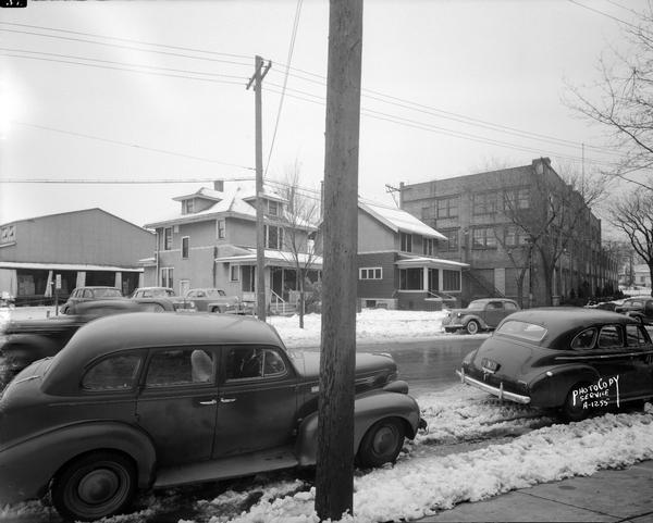 Ray-O-Vac buildings on the 2300 block of Winnebago Street. Office building, production plant, two houses: 2327 and 2331 Winnebago Street, and several cars. Snow is on the ground.