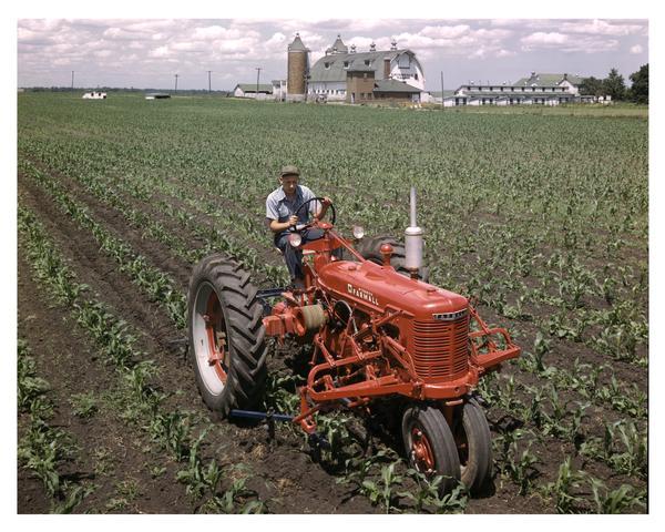Slightly elevated view of a man using a Farmall H tractor near International Harvester's experimental farm.