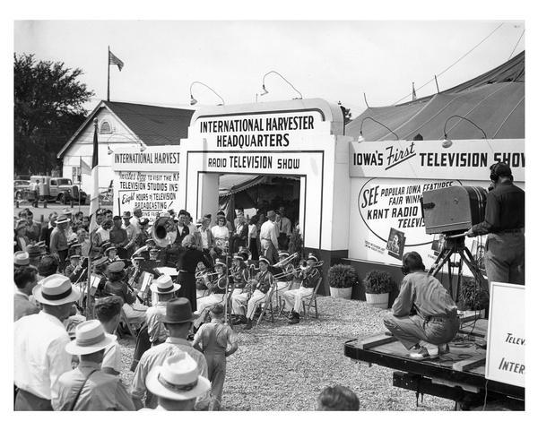 International Harvester tent and exhibition at the Iowa State Fair. Includes workers filming Iowa's first television show and a high school brass band entertaining fair-goers.