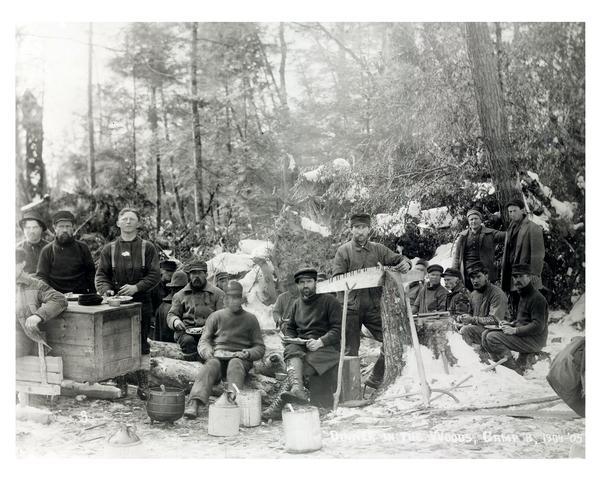 Loggers at dinner in the woods north of Glen Flora. The man in the center is filing his saw.