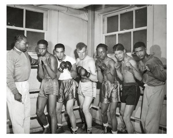 Six fighters in pugilistic poses, in the boxing ring with their coach. The Milwaukee Urban League provided community activities, like boxing, for children and adults.