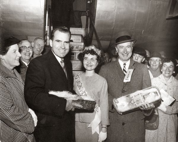 Richard M. Nixon welcomed by Barbara Bird, Honey Queen, and Wisconsin Governor Vernon W. Thomson with cheese package at the Oshkosh Airport.