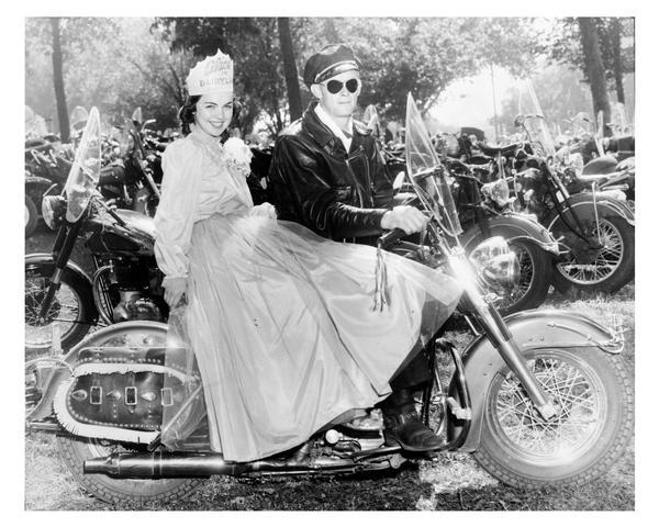 Alice in Dairyland, Marjean Czerwinski, wearing her crown and gown, rides on the back of a Harley-Davidson motorcycle.