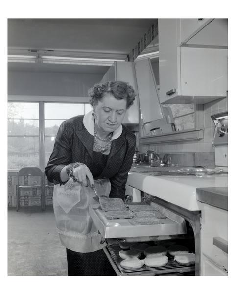 An apron-clad woman broiling hamburgers in the kitchen.