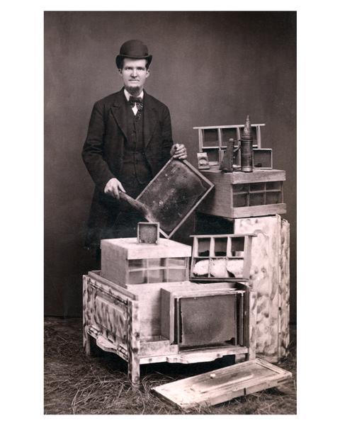 L.E. Mercer, of Lenox Iowa, posed with honey-producing equipment. Mercer is wearing a full suit, bow tie, and hat.