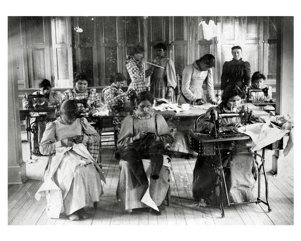 Sewing room at Lac du Flambeau U.S. Government School for Indian children. Female students posed at their sewing machines and work tables.