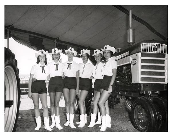 Women wearing International Harvester cowboy hats are posing in front of a Farmall 460 Tractor.