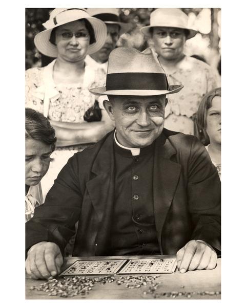 Reverend Richard Kiefer of Sacred Heart monastery in Hales Corners, Wisconsin, joins in the bingo competition at a Catholic picnic, as women and children are looking on from behind.