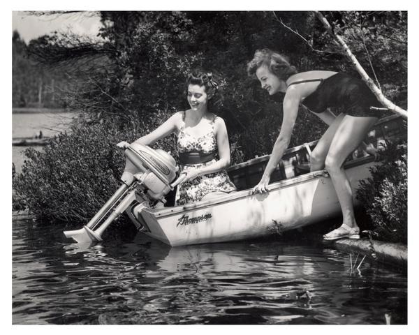 Two bathing suit-clad women demonstrating their Evinrude motorboat on a Wisconsin lake.