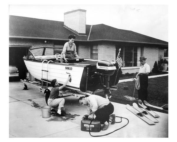 An industrious family cleans their motorboat which is parked in the driveway.