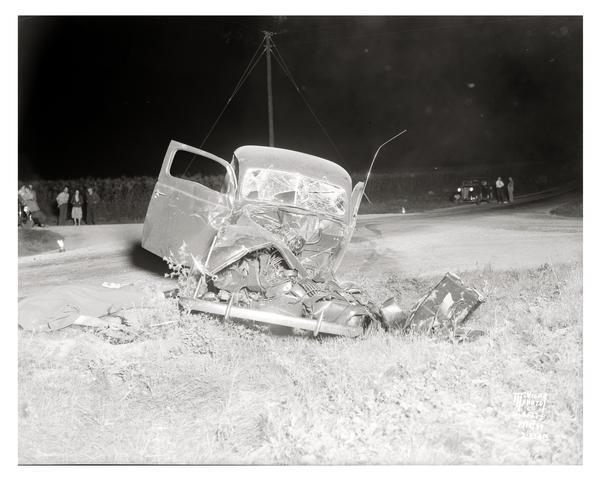 View from front of Capital City Culvert Company automobile involved in an accident with a Phillips Produce Company egg truck at the intersection of County Trunk Highway M and PB, taken at 2:35 a.m. Spectators look on from across the road. Edward F. Gafke, of Basco, died in the accident.