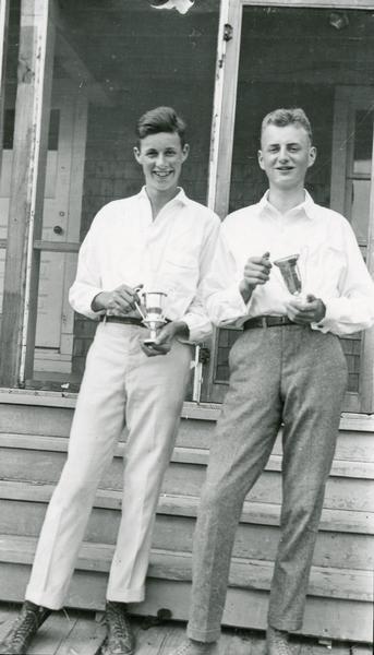 Two young men, Herbert W. Rogers and Ted Dwyer, holding trophies, standing in front of porch.