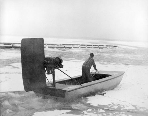 Man driving windsled on frozen Lake Superior. The windsled is an open boat fitted with an engine and rudder.