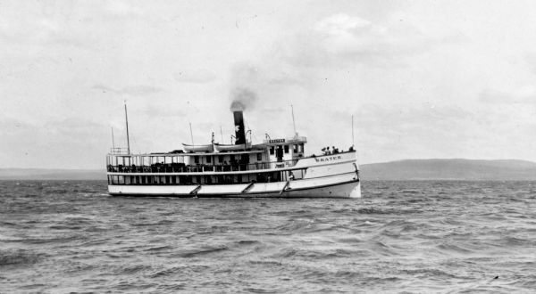 View across water of the steamboat "Skater" cruising Lake Superior, with the Bayfield bluffs in the background.