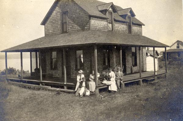 A family sits on a porch of a two-story cedar shake house with Lake Superior in background.