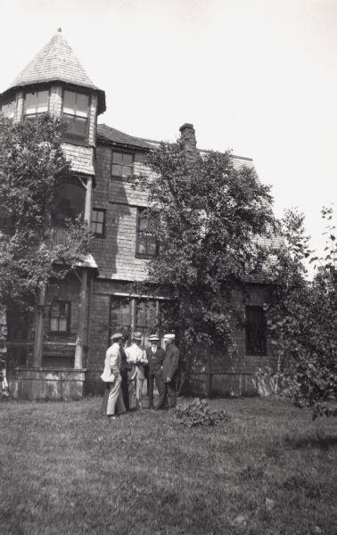 Group of five people, (includes Jesse Stone, Mrs. Abernathy, A.G. Hull, Leo Capser, and Captain Angus) standing in front of Cedar Bark Lodge on Hermit Island, Apostle Islands. Cedar Bark Lodge was also known as the Hermitage.