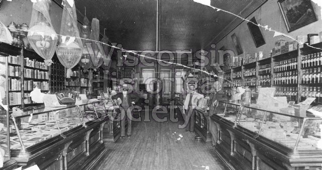 Interior view of the Kimberly & Elwers Drugstore. Pharmaceutical bottles line the shelves on the right side.