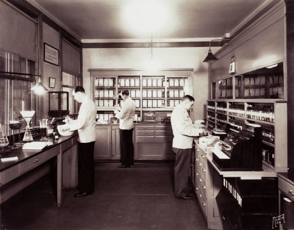 A trio of druggists busy themselves in the laboratory with compounding materials for patient prescriptions. The pharmacists were employed with "The Pharmacy," Max Lemberger, proprietor.