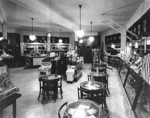 Interior of Sheehy's Pharmacy. On the left is a lunch counter and soda fountain. Customer tables are to the right, surrounded by displays for toiletries such as Colgate Fine Soaps, Cashmere Bouquet, etc.