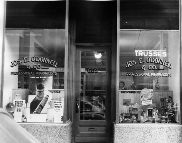 Left entrance to the O'Donnell and Company Pharmacy. The window on the left is decorated with advertisements for Squibb dental care products.
