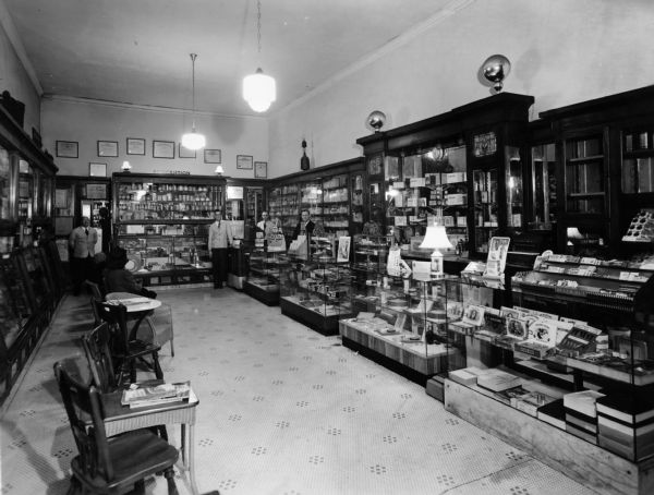 View of the interior of Cook's Drugstore. Several staff members are standing behind the counter in the store's rear. A customer waiting area is on the left.