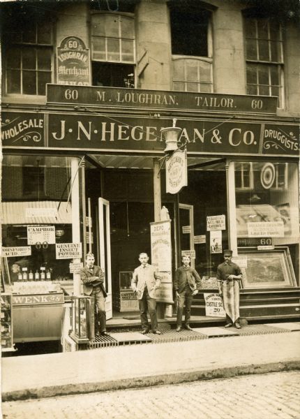 Exterior view of the J.N. Hegeman Drugstore at 60 Fulton Avenue. Left to right: a clerk, J.W. Ferris, an errand boy, William O'Bry, and a porter.