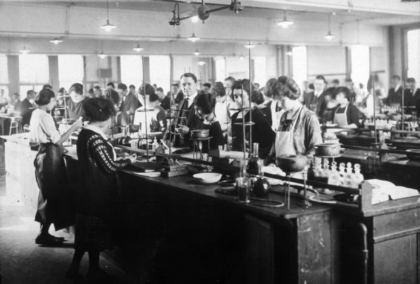 A professor checks the progress of several female students in a pharmaceutical laboratory course.