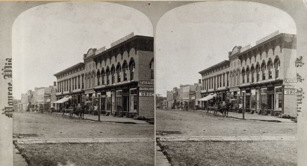 Stereograph view of downtown businesses, on the courthouse square. On the right corner is a drugstore and shoe store.