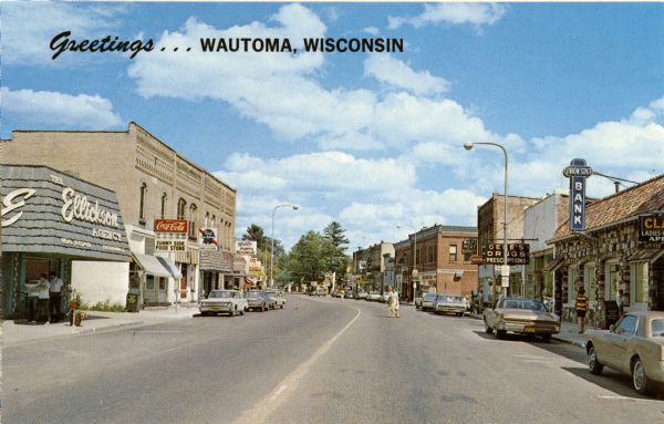 View of businesses in the Main Street area of Wautoma. Some storefronts featured are, on the right, Ellickson Agency, Sunny Side Food Store, a bar, a mens' wear store, and, on the left, Union State Bank and Gene's Drugs. Caption reads: "Greetings . . . Wautoma, Wisconsin."