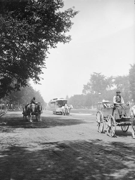 View looking up Grand Avenue from 9th Street toward two horse-drawn wagons and a horse-drawn streetcar on the tree-lined street. The wagon on the right is carrying firewood.