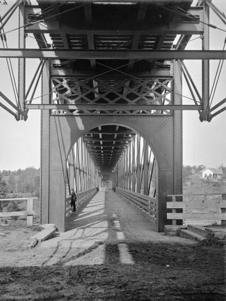 Interior of railroad bridge, with walkway below. There is a man standing on the left at the railing of the walkway.