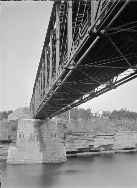 View of the river and the underside of a railroad bridge at Kilbourn. There is a building in the background on the right just above the cliffs along the river.