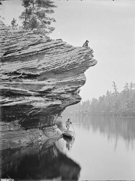 Robinson's Landing; view up the river, with a man in uniform standing in a canoe. There is a man on the ledge above.