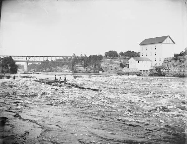 Raft over Dam at Munger's Mill View across water of several men steering a lumber raft over the dam at Munger's Mill. A second raft is in the background, in front of railroad bridge.