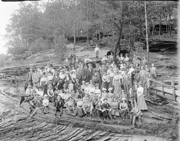 Group of men and women posing on rocks. There is a wooden bridge at right.