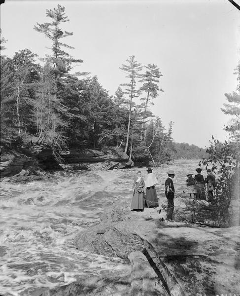 A group of people are standing on the Narrows looking at the high water. An inscription by Dells pilot Leroy Gates is visible across the river.