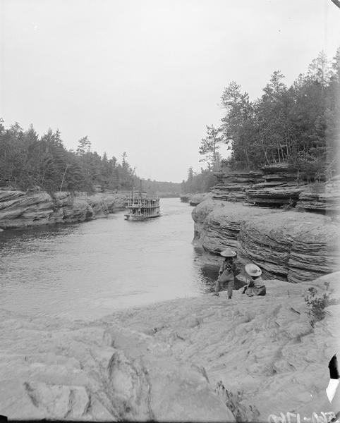 View down rock formation towards the <i>Apollo</i> steamboat at the entrance to Cold Water Canyon. Two girls are posing on the rocks in the foreground looking out towards the river.