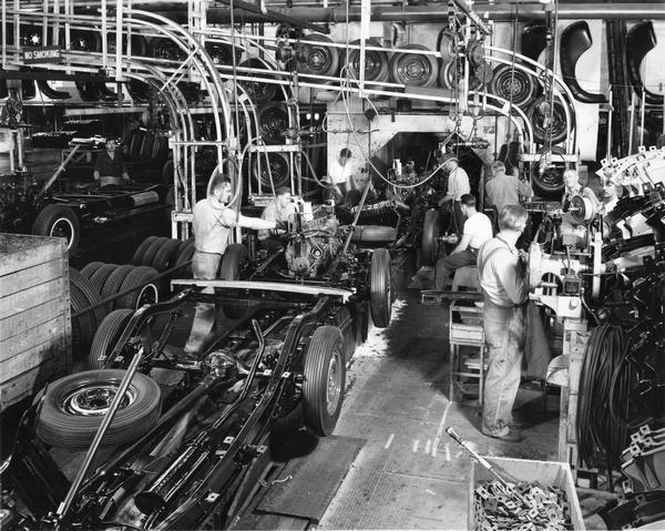 General Motors chassis assembly. Men are working among the machinery.