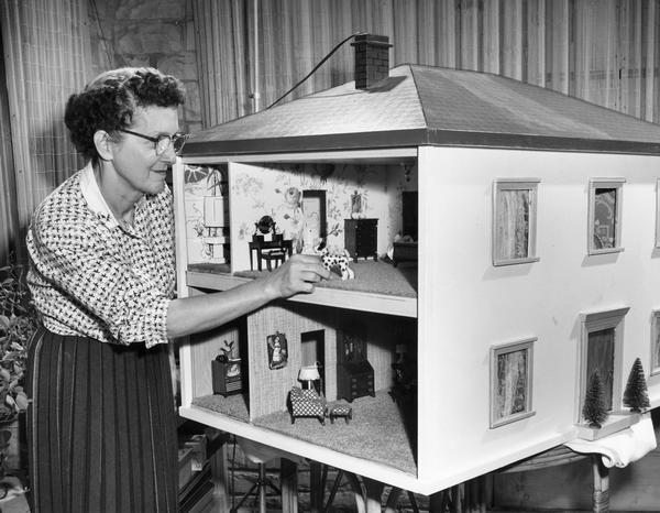 Woman making a small adjustment to an interior room in a dollhouse.